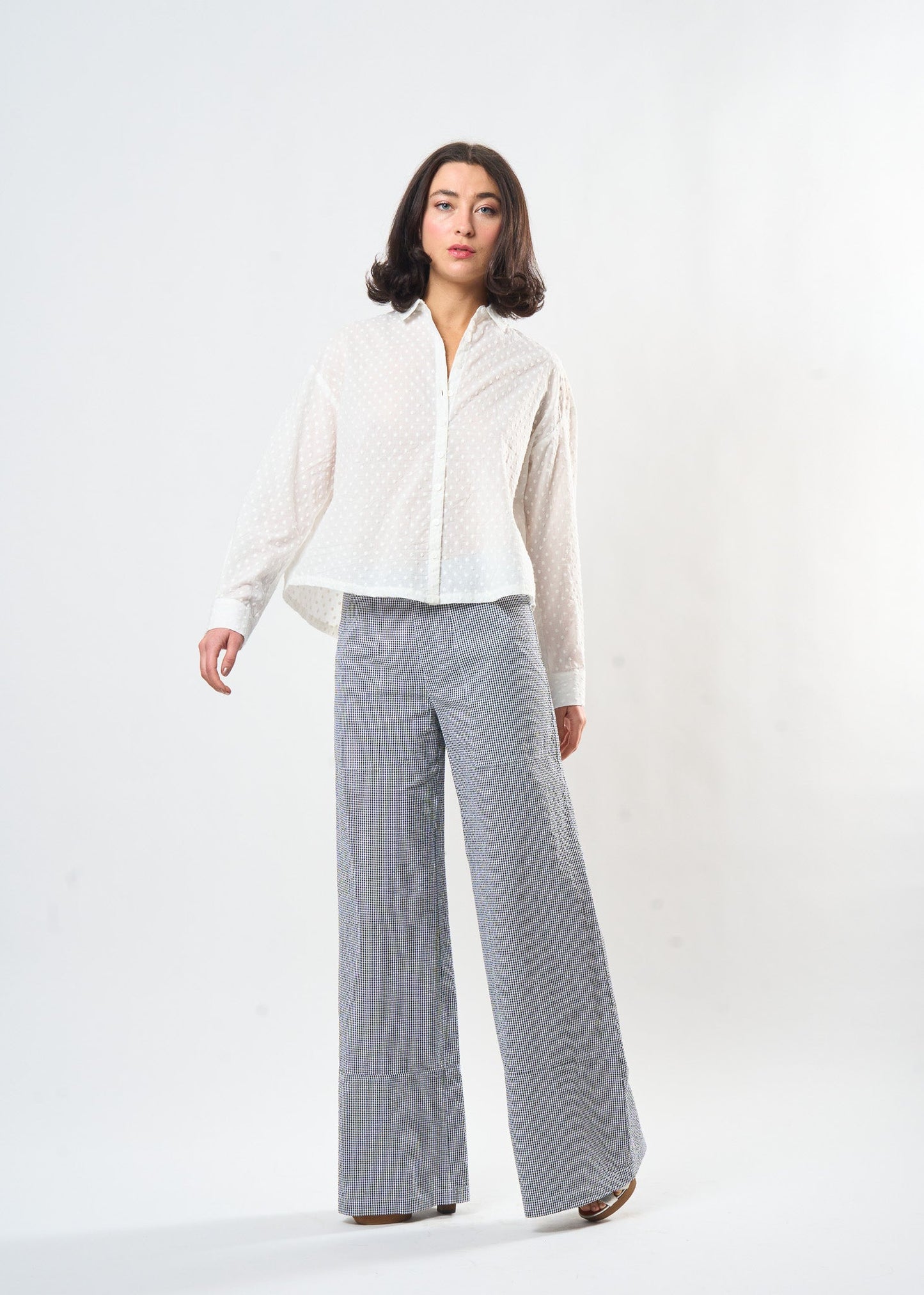 Woman wearing a white blouse and gray checkered pants on a white background