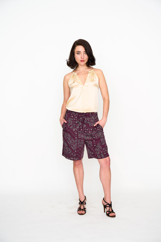 Woman wearing a light-colored silk halter top and patterned Bermuda shorts on a white background